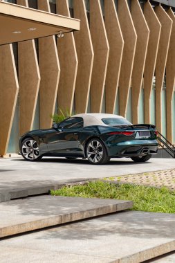 Koyu yeşil Jaguar F tipi arka üç çeyreklik kapalı beyaz kapaklı, üstü açık spor araba güneş ışığında.
