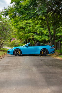 Mavi Porsche 911 Targa 4 GTS yan görüntüsü, konut bahçesinde üstü açık spor yara izi.
