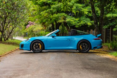 Mavi Porsche 911 Targa 4 GTS yan görüntüsü, konut bahçesinde üstü açık spor yara izi.