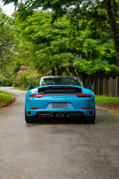 Mavi Porsche 911 Targa 4 GTS dikiz görüntüsü merkezli, lüks spor araba durağanı asfalt yolda.