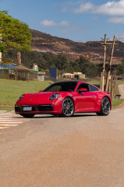 Kırmızı Porsche 911 Carrera önde üç çeyrek, taşra yolunda lüks spor araba