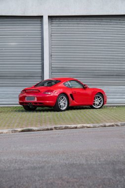 Kırmızı Porsche Cayman S arka üç çeyreklik, desenli kaldırımda lüks spor coupe.