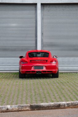 Kırmızı Porsche Cayman 'ın dikiz aynası, metal duvarın önünde lüks spor arabaları.