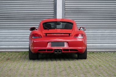 Kırmızı Porsche Cayman 'ın dikiz aynası, metal duvarın önünde lüks spor arabaları.