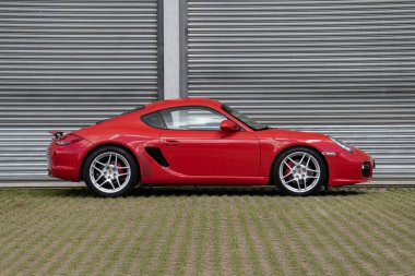 Kırmızı Porsche Cayman 'ın yan görünüşü, lüks spor arabaları endüstriyel garajın oraya park edilmiş.