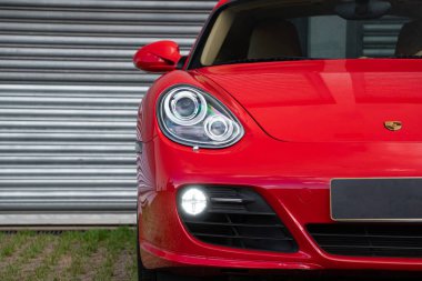 Kırmızı Porsche Cayman 's ön far ışığı odaklı çekim, metal kapının önünde lüks spor coupe