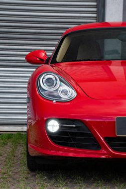 Kırmızı Porsche Cayman 's ön far ışığı odaklı çekim, metal kapının önünde lüks spor coupe