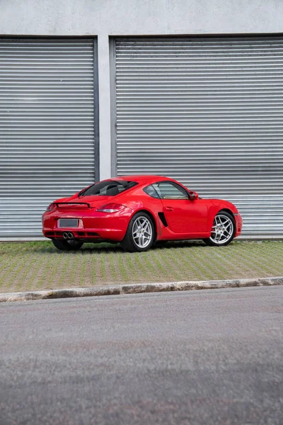 Kırmızı Porsche Cayman S arka üç çeyreklik, desenli kaldırımda lüks spor coupe.