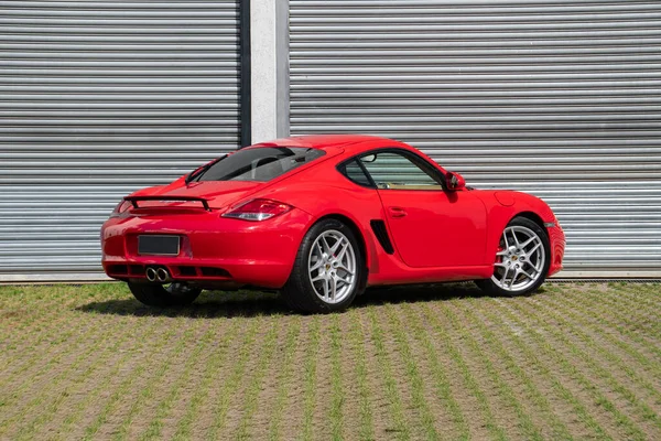 Kırmızı Porsche Cayman S arka üç çeyreklik, desenli kaldırımda lüks spor coupe.