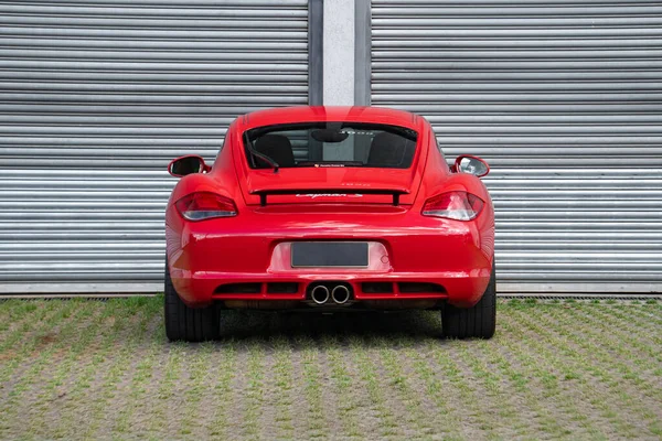 Kırmızı Porsche Cayman 'ın dikiz aynası, metal duvarın önünde lüks spor arabaları.