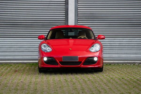 Kırmızı Porsche Cayman S ön manzara, metal garaj kapısının önünde lüks spor coupe.