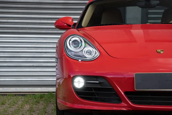 Kırmızı Porsche Cayman 's ön far ışığı odaklı çekim, metal kapının önünde lüks spor coupe