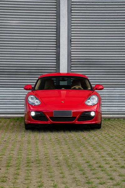 Kırmızı Porsche Cayman S ön manzara, metal garaj kapısının önünde lüks spor coupe.