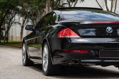 Siyah BMW 650i arka manzara, lüks arka taraf manzarası ağaç çizgili yolda.