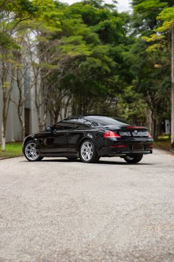 Siyah BMW 650i arka üç çeyrek görüş, boş yolda lüks coupe ağaçlarla çevrili