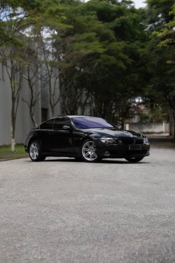 Siyah BMW 650i ön manzara üç çeyrek, lüks sedan ağaçlı yolda bulutlu bir günde park edilmiş.