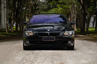 Siyah BMW 650i önden görüş, boş ağaç üzerinde lüks coupe güneş ışığı gölgeli yol.