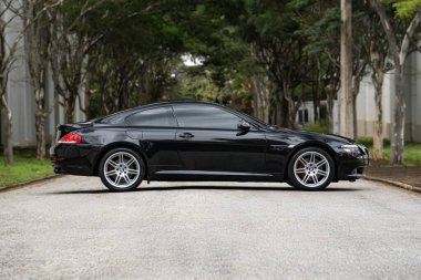 Siyah BMW 650i yan görünüm, yemyeşil ağaçlarla dolu boş yolda lüks coupe.