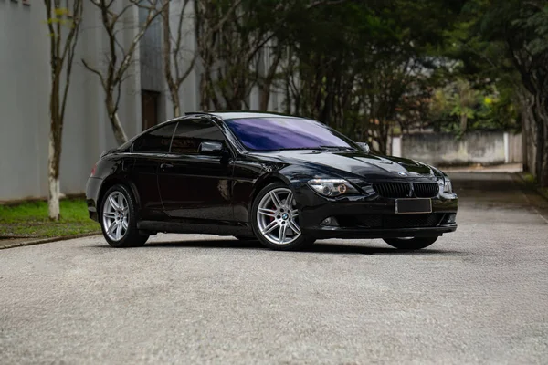 Siyah BMW 650i ön manzara üç çeyrek, lüks sedan ağaçlı yolda bulutlu bir günde park edilmiş.