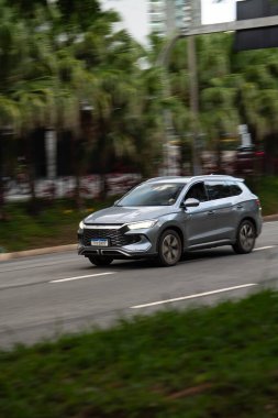 Gümüş rengi BYD Song Plus hareket halinde, Melez SUV şehir yolunda hareket bulanıklığı ile sürüyor.