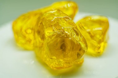 Parlak sarı jelibonlar sade bir tabağa konur. Birçok insan bu tatlıları atıştırmalık ya da tatlı olarak sever. Farklı şekillerde ve tatlarda geliyorlar, bu da onları popüler yapıyor. Makro kehribar.