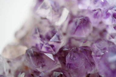 Ametist kristalleri, belirgin şekillerini ve mor tonlarını vurgulayan yakın çekim bir görüntüde sergilenir. Doğal ışık yüzlerden yansıyarak güzelliklerini gösterir..