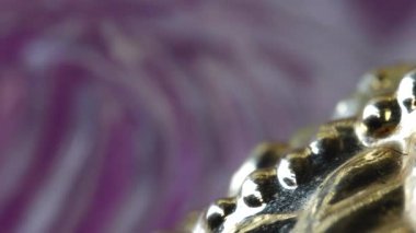 Sahne parlak metalik bir nesneyi gösteriyor. Detaylı, desenli bir yüzeyi var. Renkli bir arkaplanda serili. Işık objeden yansıyarak özelliklerini vurgular. Kapalı görünüm, desenli bir tasarımı olan metalik bir nesnenin ayrıntılarını gösterir