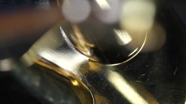Bir kişi atölyedeki bir aleti kullanarak pirinç bir nesneyi parlatıyor. İşçi işe odaklanırken parlak yüzey ışığı yansıtır. Gündüz vakti ve bölge oldukça dar. Atölyede parlayan parlak pirinç bir nesneye yakından bakın..