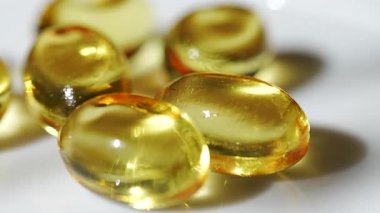 Altın kapsüller beyaz bir yüzeyde doğal ışık altında sıcak sarı bir zemin ile düzenlenir. Altın kapsüller beyaz bir yüzeyde duruyor. Şekerler parlak ve altın sarısı. Sarı arkaplan sıcak ışık sağlar.