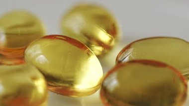 Altın kapsüller beyaz bir yüzeyde doğal ışık altında sıcak sarı bir zemin ile düzenlenir. Altın kapsüller beyaz bir yüzeyde duruyor. Şekerler parlak ve altın sarısı. Sarı arkaplan sıcak ışık sağlar.