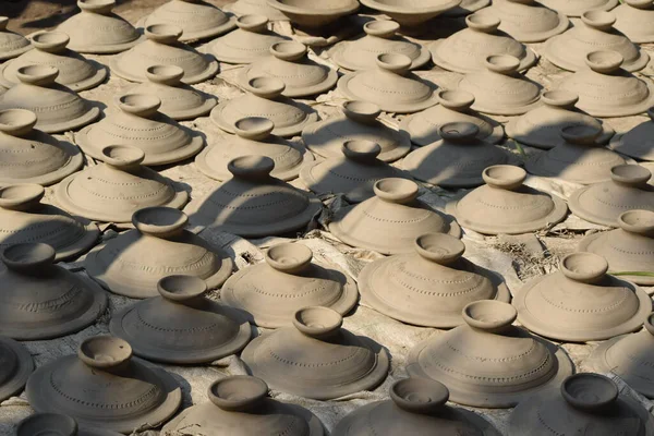 Sayısız işlenmemiş kil tencere kapakları güneşin altında kurumak üzere sıralanmış..
