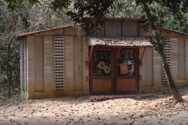 Küçük, kırsal bir binanın önünde, muhtemelen bir dükkan ya da konut, eğimli teneke bir çatı, beton bloklar ve ahşap panellerden yapılmış duvarlar. Yapının çift ahşap kapısı ve cam panelleri var..