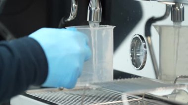 Kahve makinesinden fincana akan sıcak suyun yakın plan çekimi. Su akarken buhar yavaşça yükselir. Sıcaklığı, hassasiyeti ve demleme sürecini vurgular.