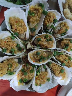 Beyaz tabakta servis edilen sarımsaklı ve yeşil soğanlı ızgara istiridye.