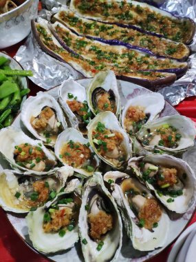 Izgara istiridye, sarımsak ve otla birlikte beyaz tabakta patlıcan ve yeşil fasulye ile servis edilir.