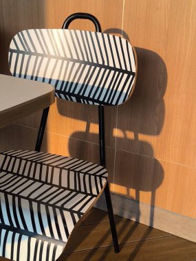 Siyah beyaz çizgili modern sandalye ahşap duvara gölge düşürüyor.