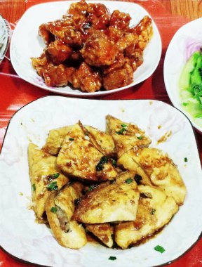 Beyaz tabakta kızarmış tavuk ve ızgara balık ve kırmızı masada garnitür.