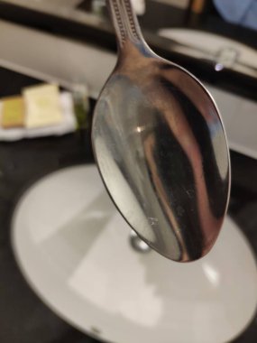 Yansıtıcı yüzeyi ve mutfak arka planı olan beyaz lavabonun üzerinde asılı parlak metal kaşık.