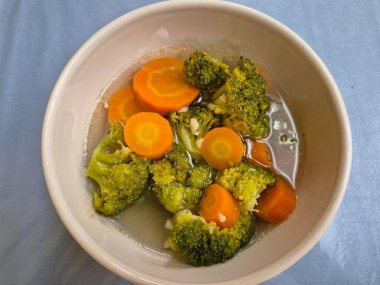 Beyaz bir seramik kasede servis edilen brokoli ve havuç sebze çorbası.