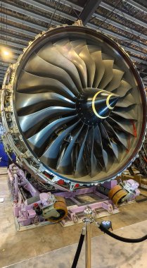 Rolls Royce Trent XWB jet motorunun bir havacılık tesisinde mobil destek karesine monte edilmiş görüntüsü. Dairesel pervane bıçakları, uzay mühendisliğinin karmaşıklığını gösteren sarı işaretli merkezi bir koninin etrafını sarar..