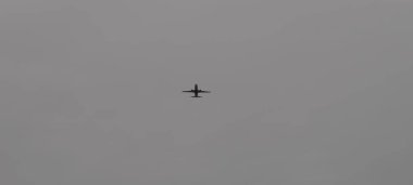 Bulutlu ve bulutlu bir gökyüzüne bakan ticari bir jet uçağının dramatik silueti. Aşağıdan yakalanan görüntü, uçakların kanatlarını, motorlarını ve kuyruğunu vurguluyor. Havacılık teması için ideal..