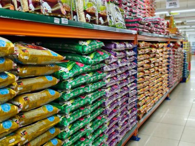 Sabah, Malezya - 25 Ocak 2026: Yerden tavana pirinç torbalarıyla dolu bir süpermarket koridorunun geniş açılı perspektifi. Çuvallar farklı gr tiplerini temsil eden çeşitli canlı renkler (yeşil, mor, sarı) ve markalaşma özelliklerine sahiptir.