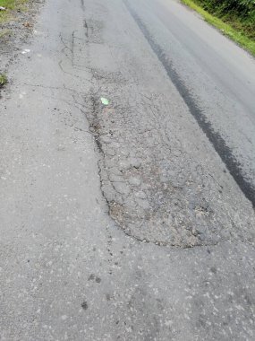 Ağır hasar görmüş asfalt bir yolun yüksek açılı çekimi büyük bir çukur ve geniş bir çatlak içeriyor. Bu resim zayıf altyapıyı, yol bakım ihtiyaçlarını ve tehlikeli sürüş koşullarını gösteriyor