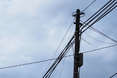 Bu yakın plan yıpranmış ahşap bir elektrik direğini yakalıyor. Karmaşık bir elektrik hattı ve kablo ağını destekliyor. Kasvetli ve bulutlu bir gökyüzüne karşı kurulmuş.