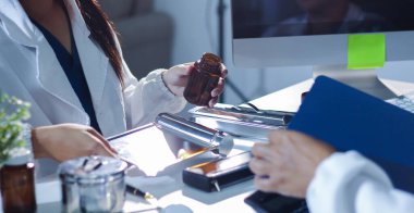 Tıbbi ekip, beyaz laboratuvar önlüklü ve ameliyat önlüklü doktorlarla toplantı yapıyor. Masada oturmuş, internette çalışan hastaları tartışıyorlar. Tıp endüstrisinde bilgisayar kullanıyorlar..