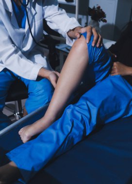 Asyalı erkek doktor hastane odasında yatağında oturan kadın hastayı muayene ediyor. Sağlık kontrolü yapıyorum. Teşhis yaralanması. Sağlık hizmeti sağlıyorum. Ayak hastalıkları. Fizik tedavi. Ve rehabilitasyon