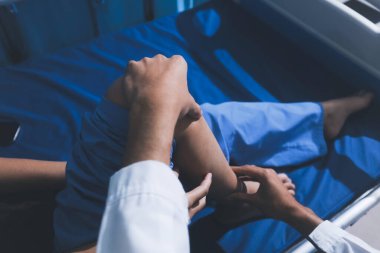 Asyalı erkek doktor hastane odasında yatağında oturan kadın hastayı muayene ediyor. Sağlık kontrolü yapıyorum. Teşhis yaralanması. Sağlık hizmeti sağlıyorum. Ayak hastalıkları. Fizik tedavi. Ve rehabilitasyon