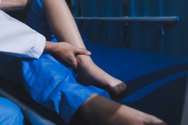 Asyalı erkek doktor hastane odasında yatağında oturan kadın hastayı muayene ediyor. Sağlık kontrolü yapıyorum. Teşhis yaralanması. Sağlık hizmeti sağlıyorum. Ayak hastalıkları. Fizik tedavi. Ve rehabilitasyon