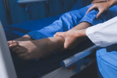 Asyalı erkek doktor hastane odasında yatağında oturan kadın hastayı muayene ediyor. Sağlık kontrolü yapıyorum. Teşhis yaralanması. Sağlık hizmeti sağlıyorum. Ayak hastalıkları. Fizik tedavi. Ve rehabilitasyon