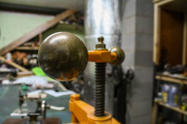 Ucunda pirinç toplar olan turuncu bir el baskısının yakın görüntüsü, atölye ortamında fotoğraflanmış. Yıpranmış yüzey, metal ayrıntılar ve endüstriyel çevre işlevsel tasarım araçlarını ve el sanatlarının atmosferini vurgular